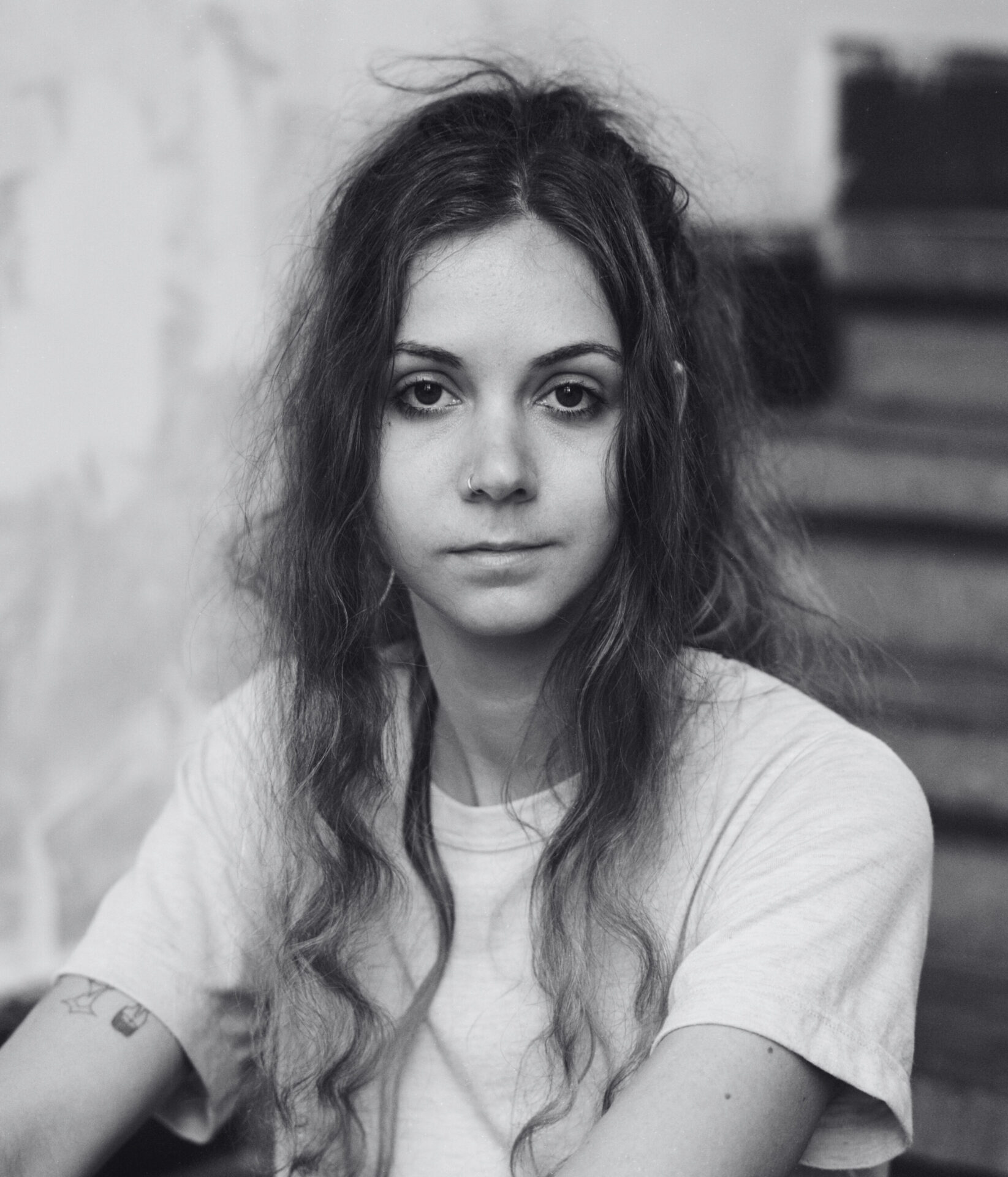 A black-and-white portrait of Dominique De Groen on the stairs, looking kindly into the camera. Een zwart-witportret van Dominique de Groen op de trap, die vriendelijk in de camera kijkt.