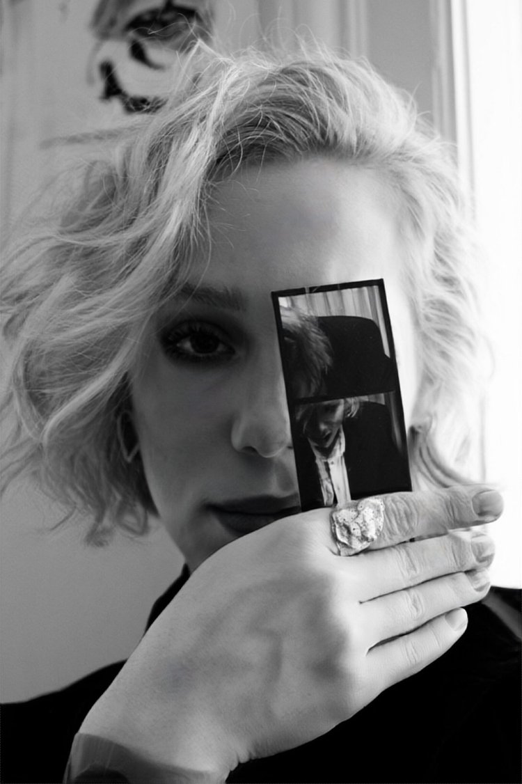 A black-and-white portrait of Hannah K. Bründl looking into the camera with a Polaroid held before her left eye. Een zwart-witportret van Hannah K. Bründl die in de camera kijkt met een Polaroid voor haar linker oog.