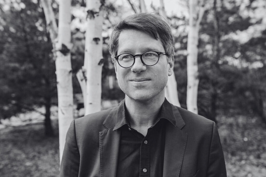 A black-and-white portret of Jan Wagner in a forest. Een zwart-witportret van Jan Wagner in een bos.