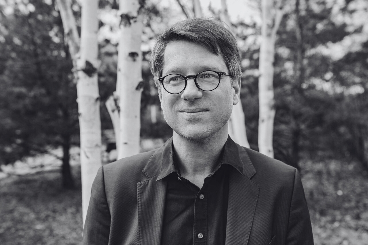 A black-and-white portret of Jan Wagner in a forest. Een zwart-witportret van Jan Wagner in een bos.