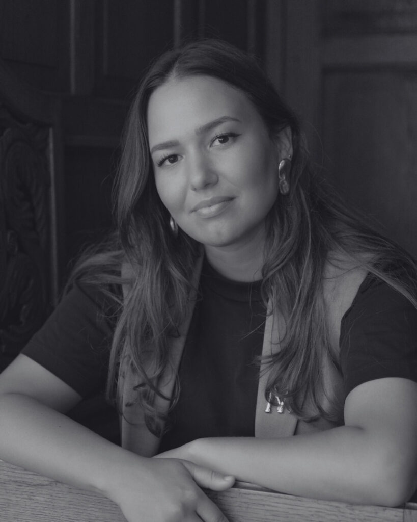 A black-and-white picture of Myriem El Kaddouri smiling at the camera. Een zwart-witfoto van Myriem el Kaddouri die naar een camera glimlacht.