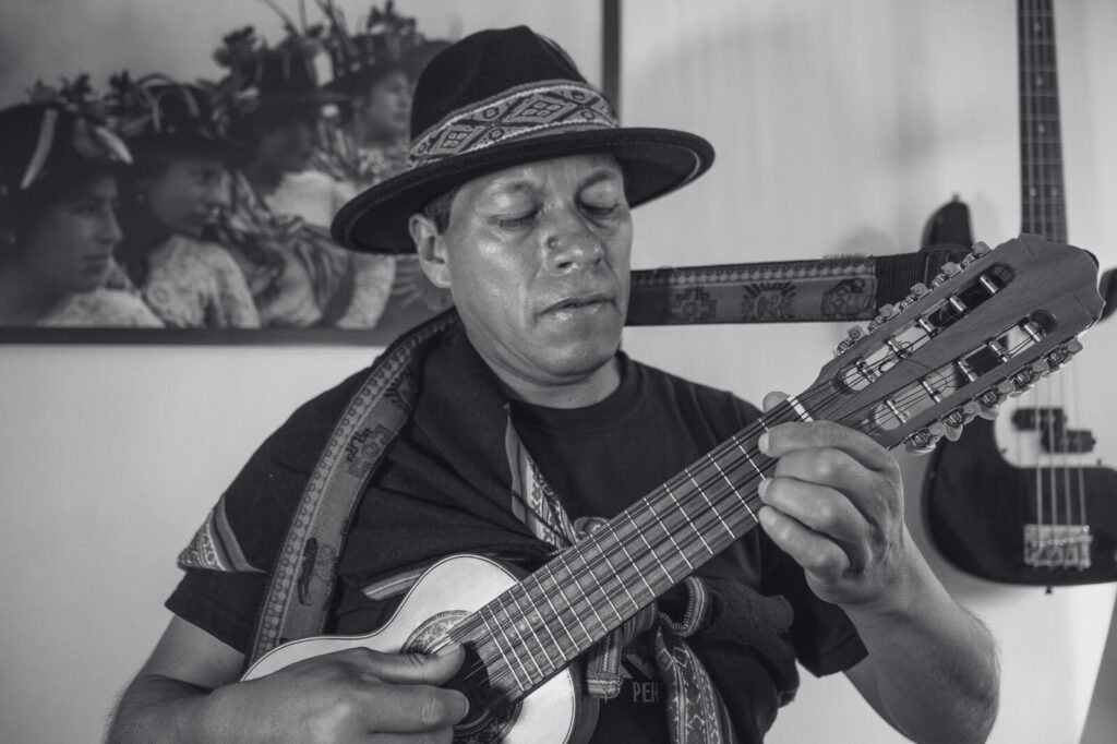 A black-and-whitepicture of Raúl Cisneros playing a charango. Een zwart-witfoto van Raúl Cisneros die een charango speelt.