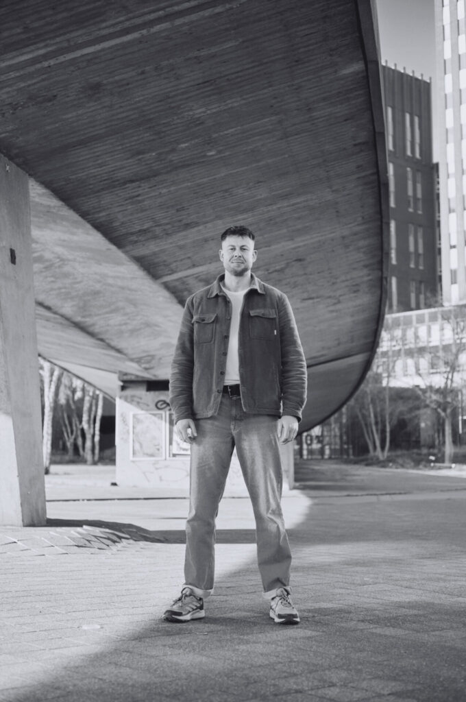 A black-and-white picture of Wessel Kootwijk standing under a bridge. Een zwart-witfoto van Wessel Klootwijk die onder een brug staat.