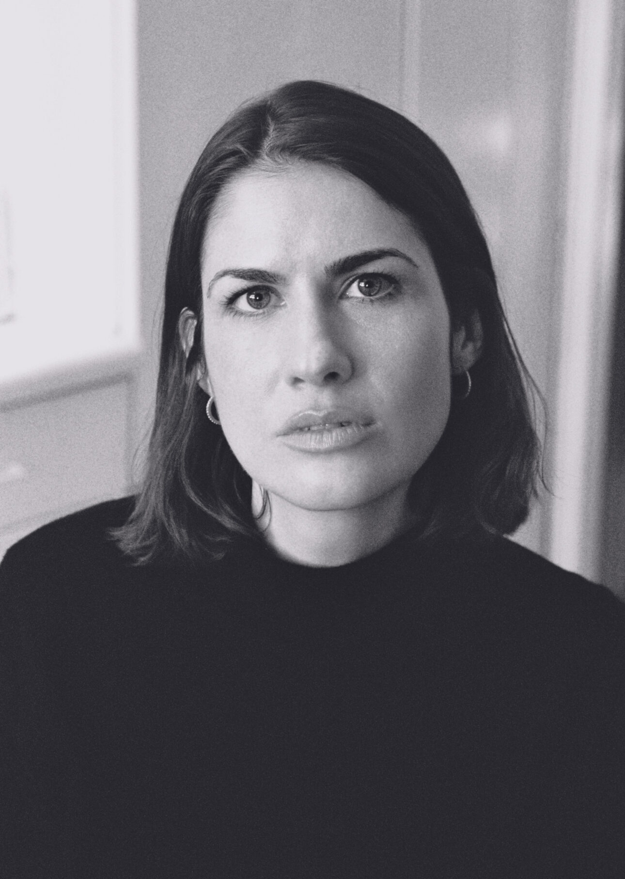 A black-and-white picture of Sarah de Koning looking at the camera. Een zwart-witfoto van Sarah de Koning die naar de camera kijkt.