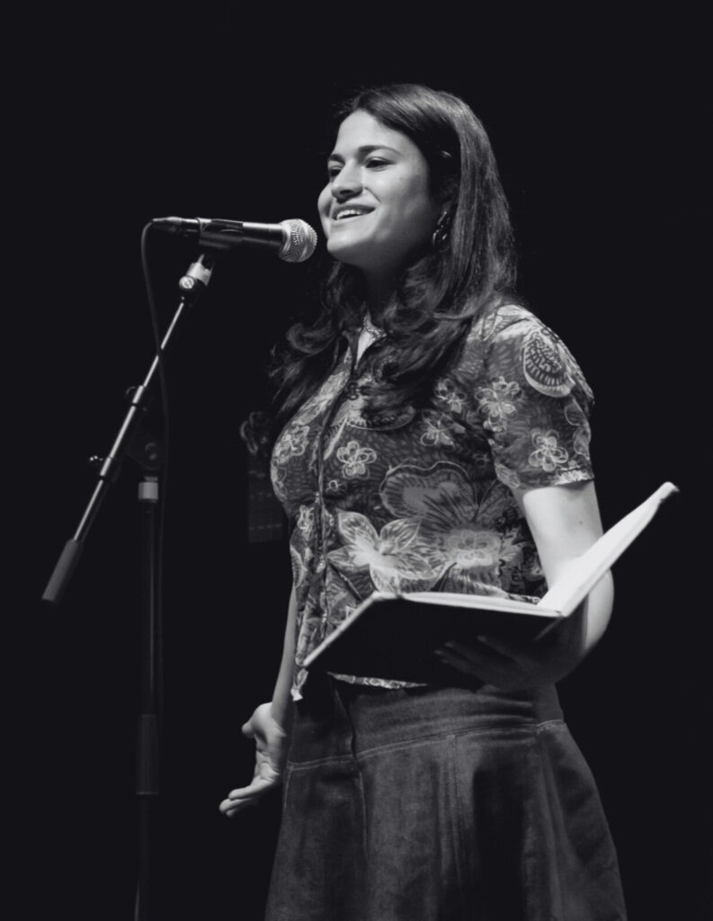 A black-and-white picture of Salma Ali performing with a book in hand. Een zwart-witfoto van Salma Ali die optreedt met een boek in hand.