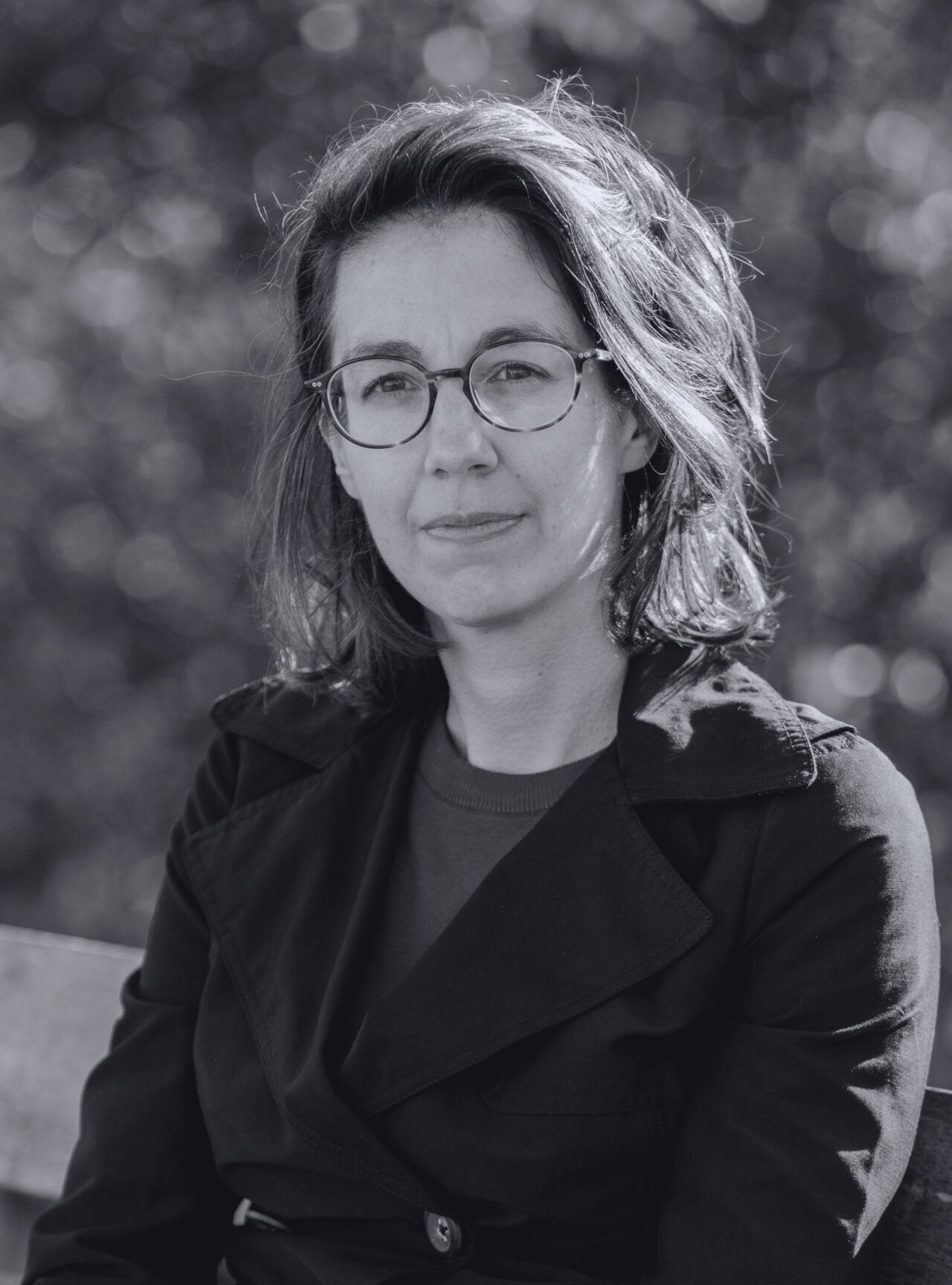 A black-and-white picture of Yasmin Namavar sitting on a bench. Een zwart-witfoto van Yasmin Namavar die op een bankje zit.
